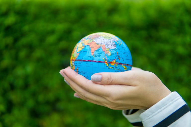 Close-up of hands gently cradling a miniature globe against a green backdrop.