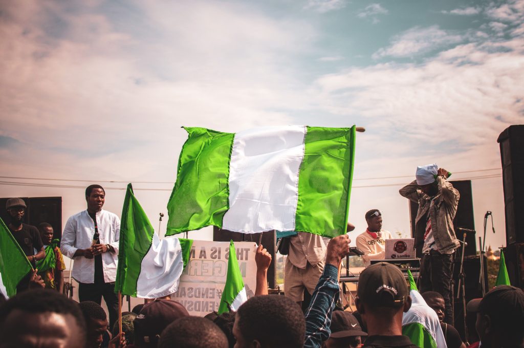 A vibrant gathering of people holding Nigerian flags outdoors under a sunny sky.